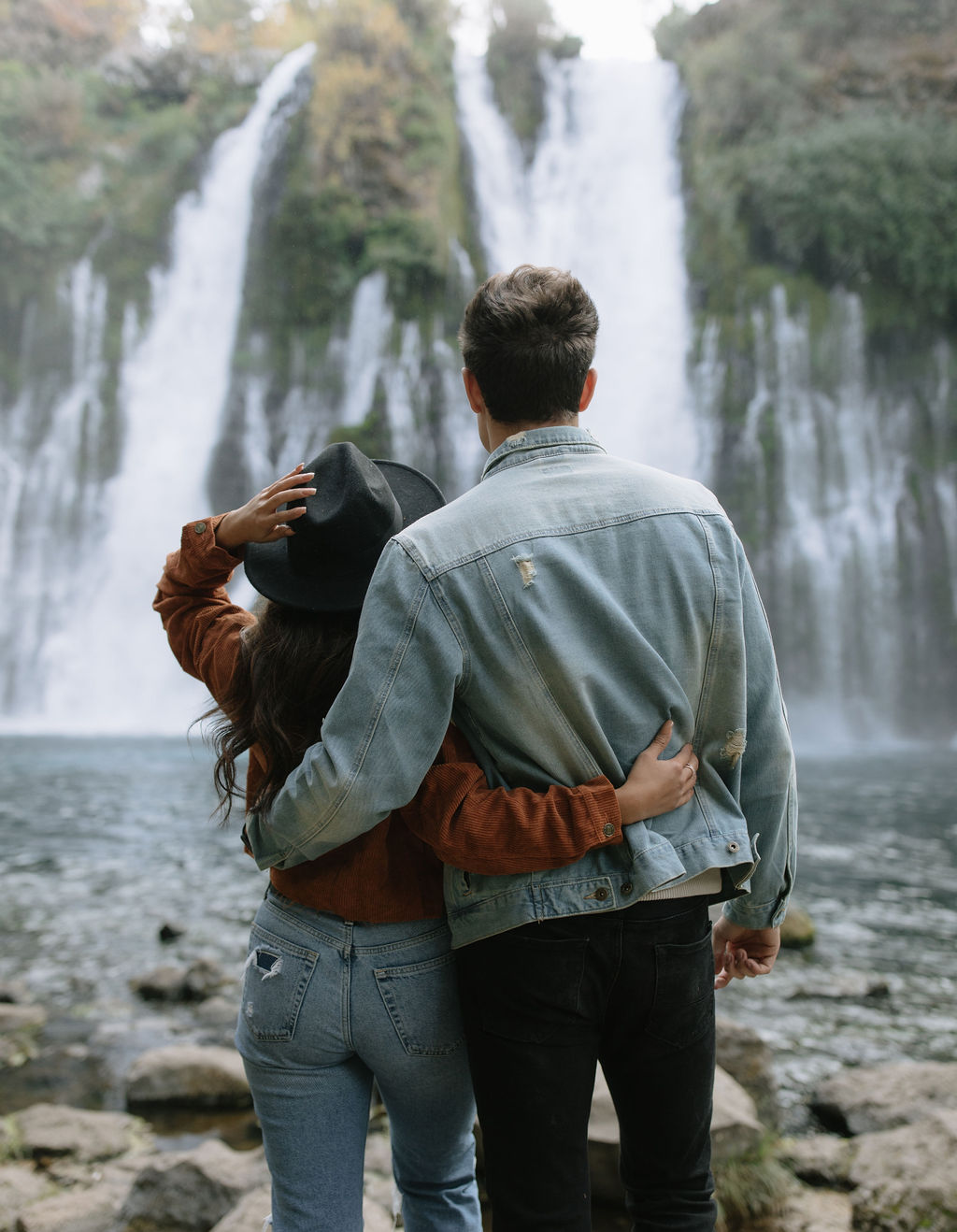 Couple looking towards waterfalls at burney falls in their engagement photos