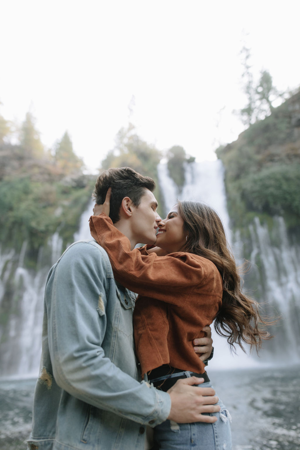 Couple going in for a kiss in front of Burney Falls