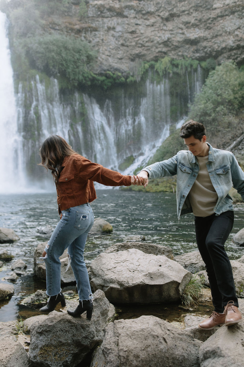 Couple holding hands and walking on the rocks at Burney Falls