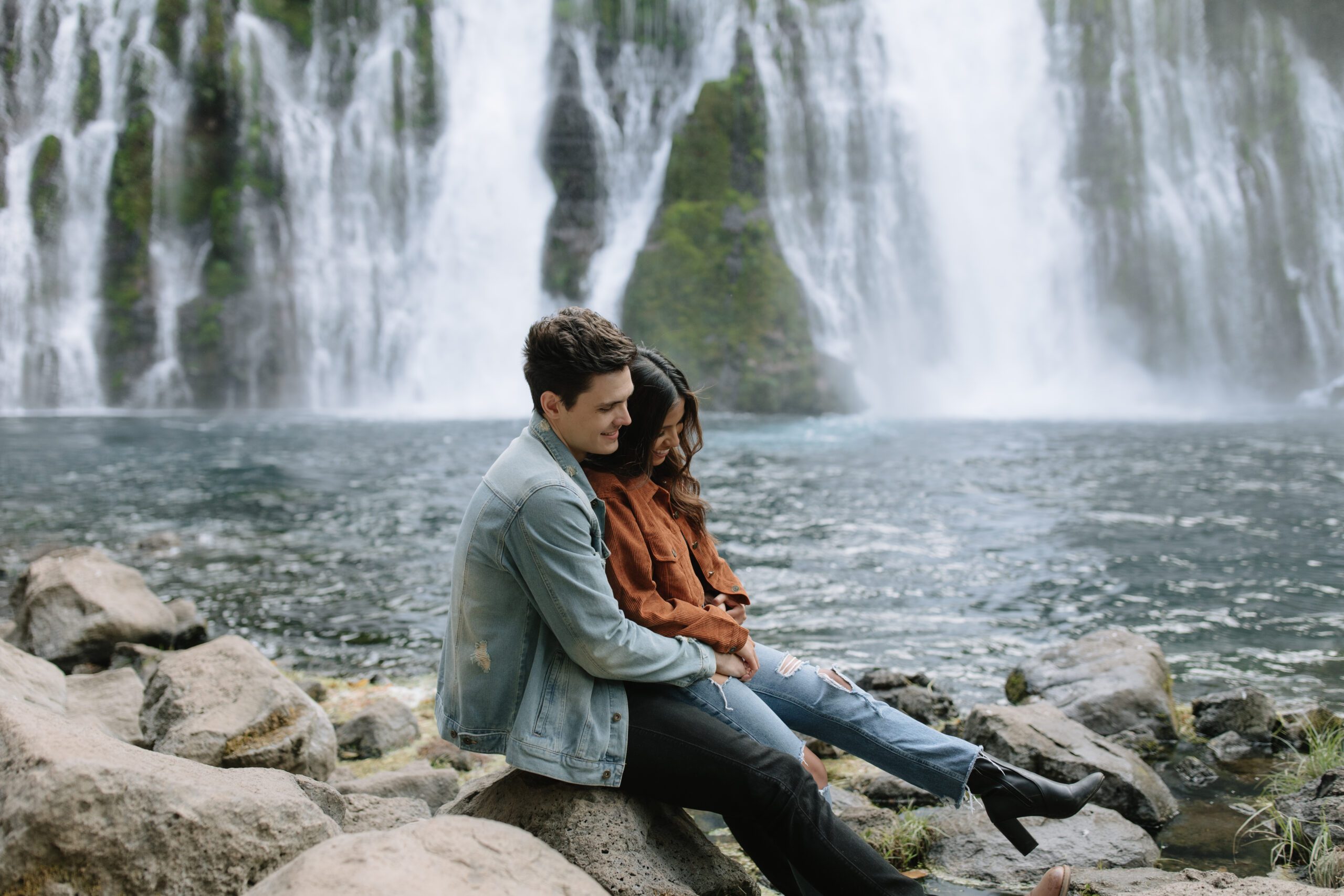 Couple sitting on the rocks together in front of Burney Falls waterfalls