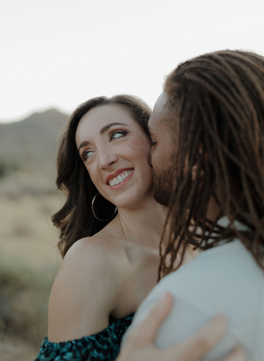 A man kissing his fiancee on the cheek in a desert