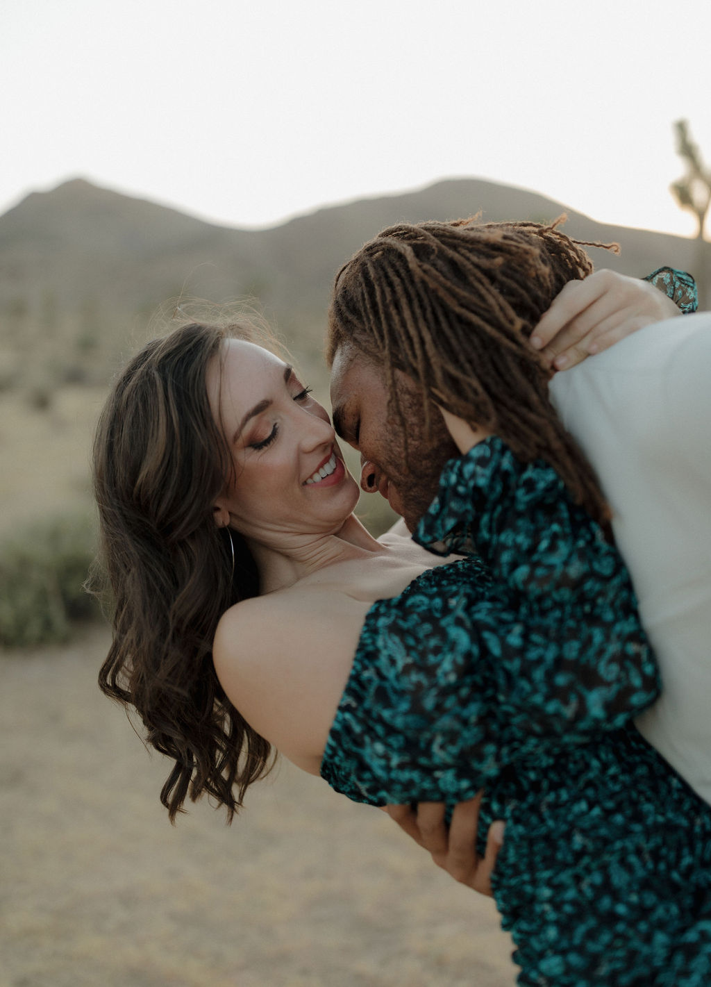 A man leaning in to kiss his fiancee for a Joshua tree photoshoot