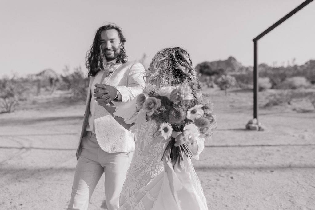 A brde and groom holding hands in Joshua tree at a boho wedding