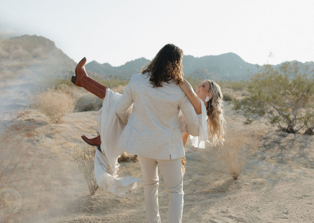 A groom carrying a bride through Joshua tree