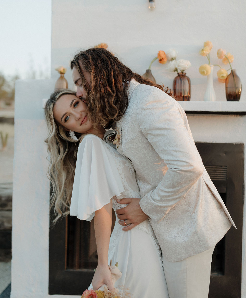 A groom kissing a bride on the cheek at a boho wedding at Joshua Tree