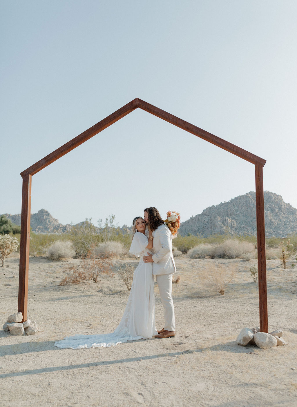A bride and groom under a boho wedding arch