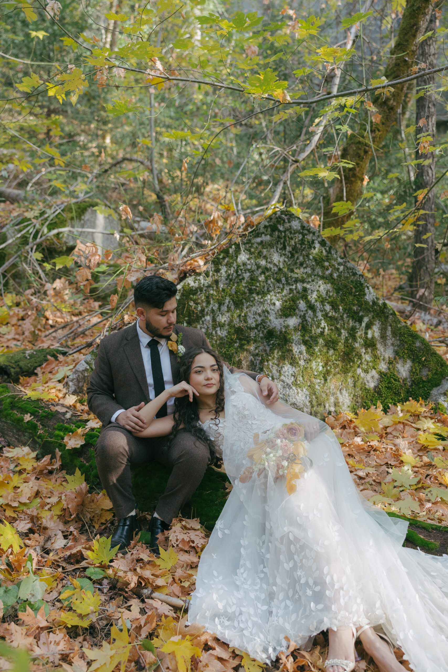 Bride and groom sitting on the ground at Yosemite national Park with fall leaves posing for a photo
