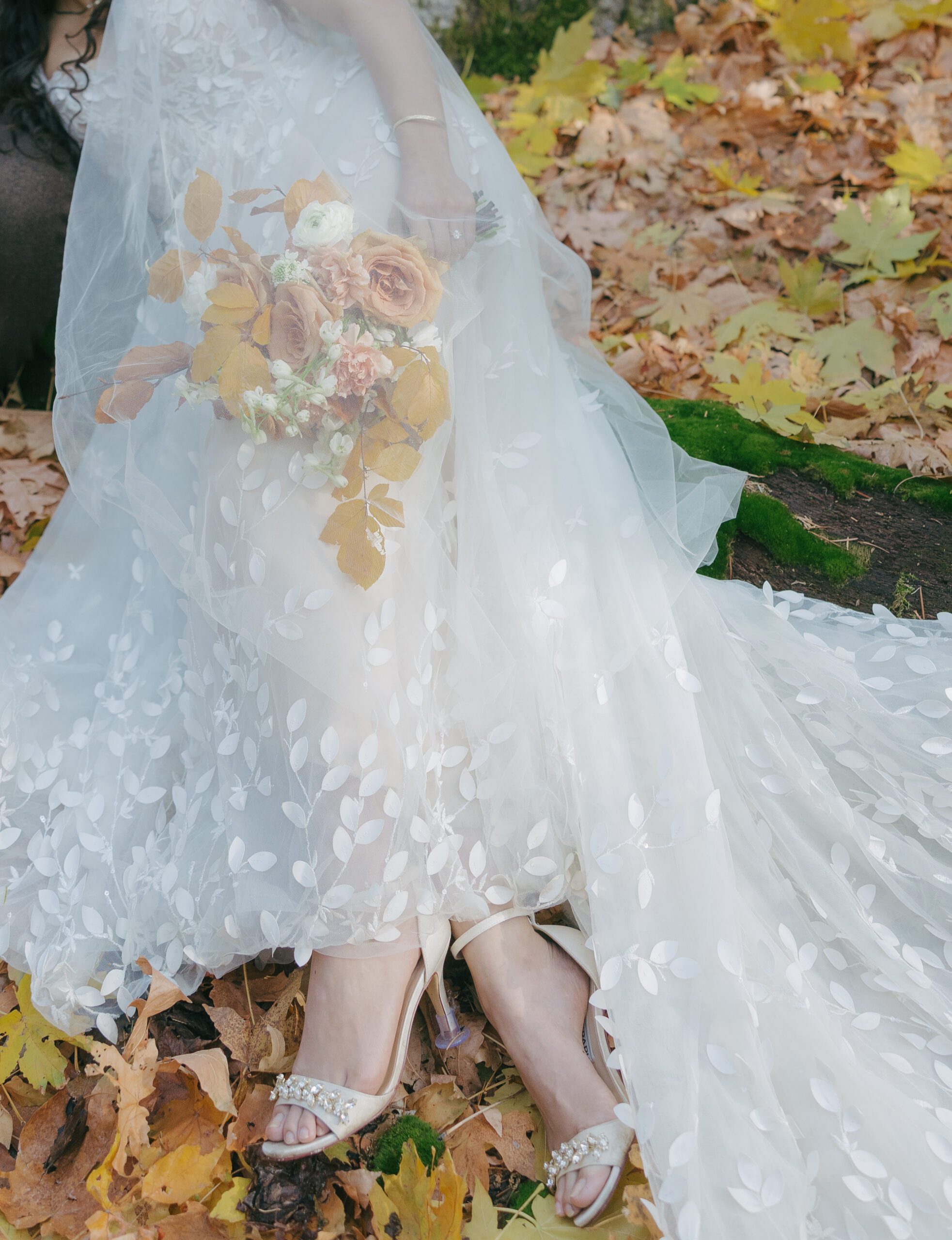 Wedding detail photos of brides wedding dress and bridal bouquet with fall leaves on the ground
