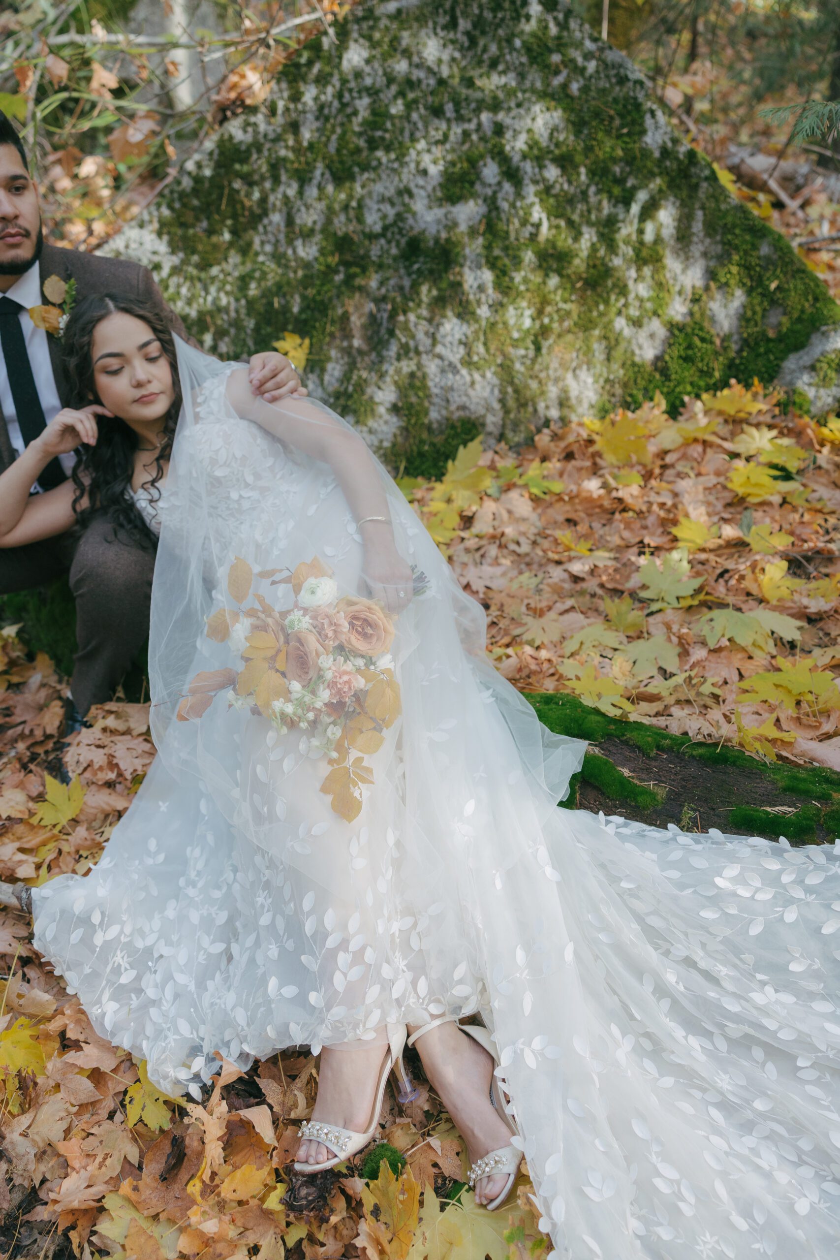 Bride and groom sitting beside rock on fall leaves with fall wedding bouquet at Yosemite
