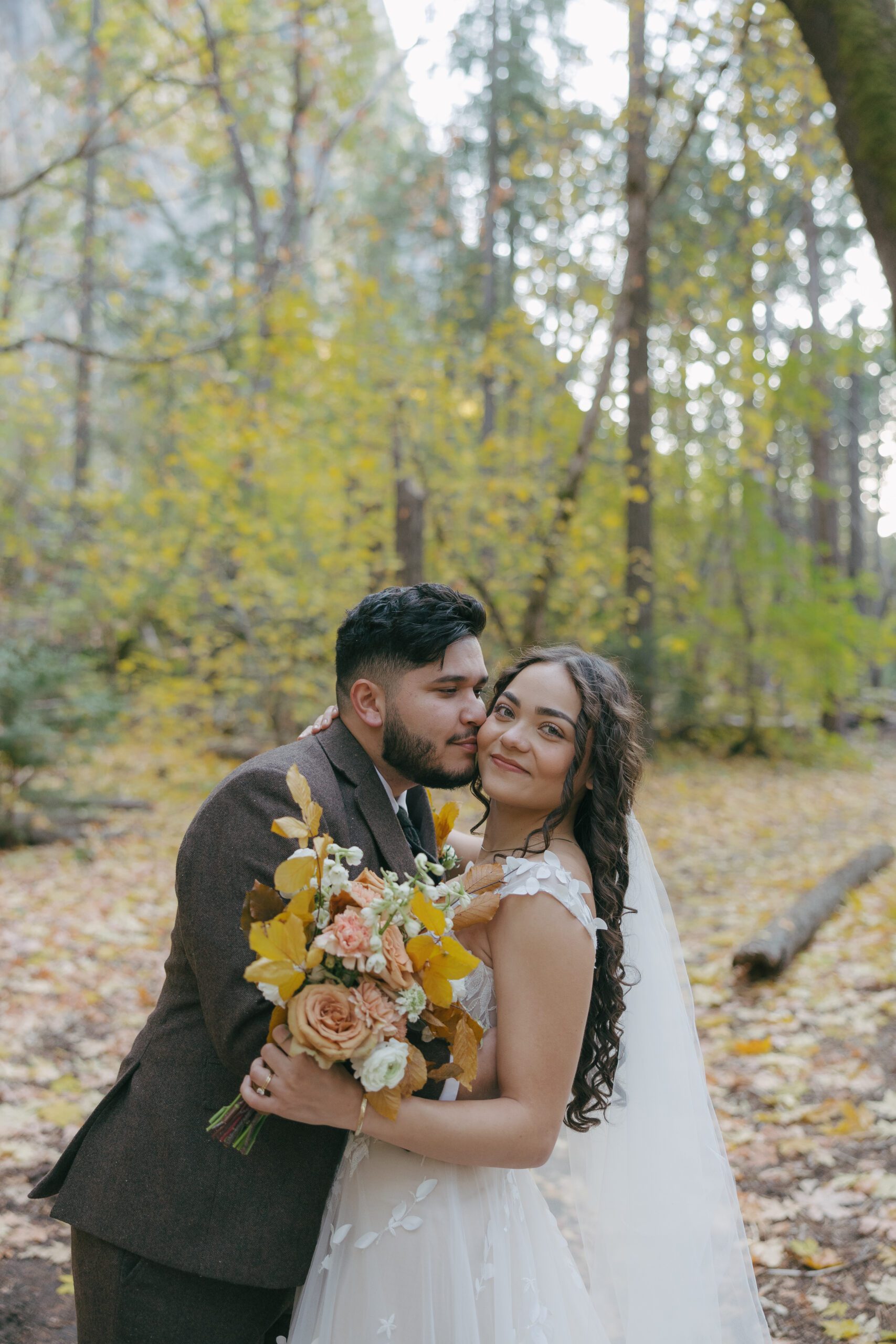 Bride and groom photo of groom kissing bride on cheek with fall wedding bouquet