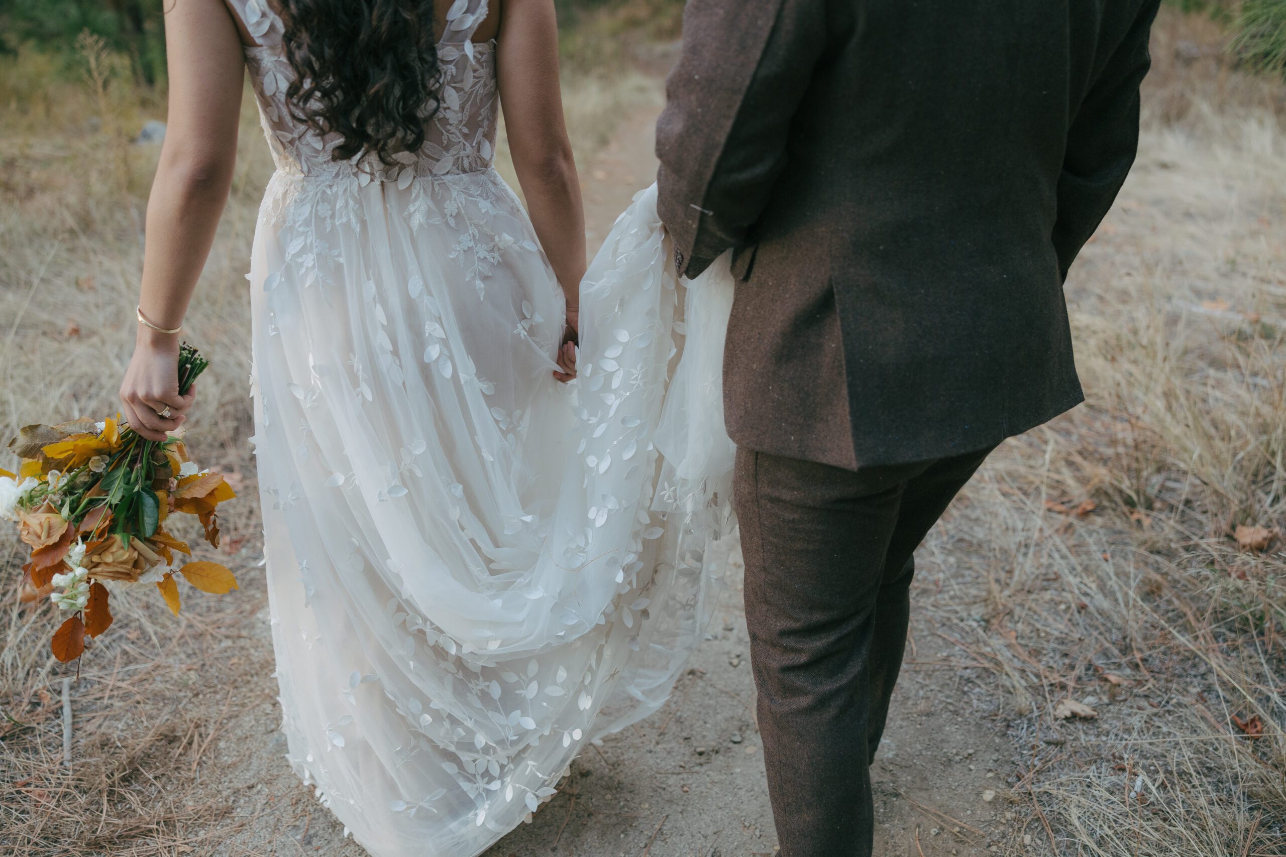 Bride and groom walking during Yosemite wedding with groom holding the train of the bride's wedding dress