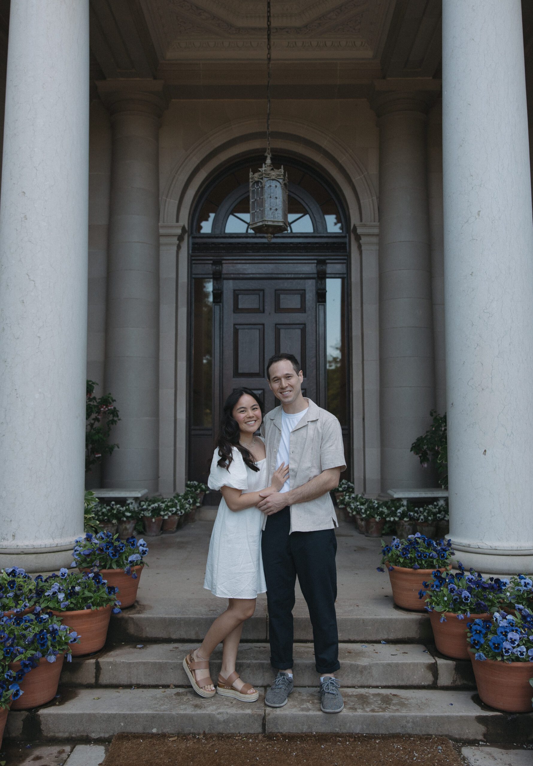 Couple standing between arches in front of historic house engagement photos