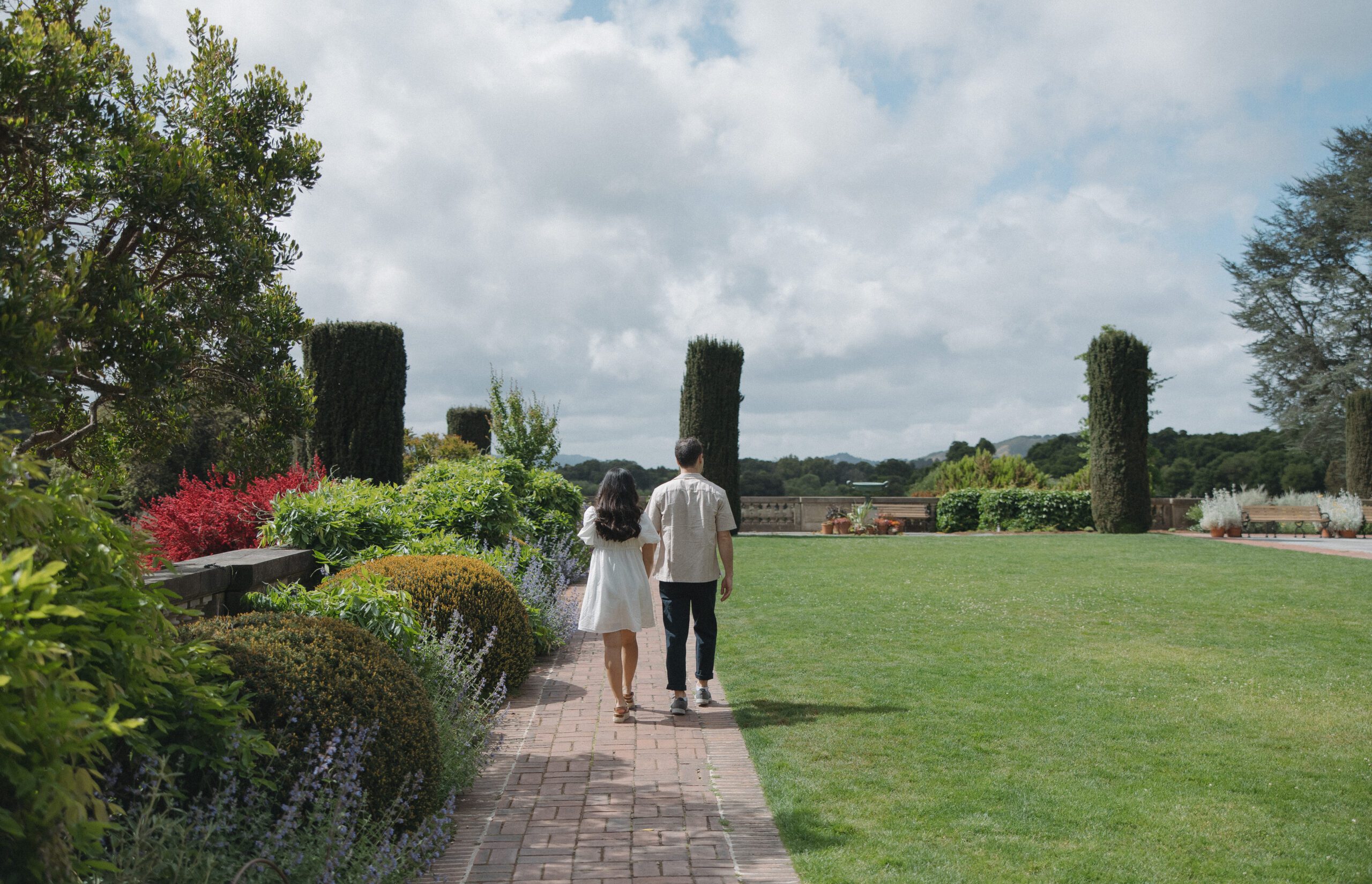 Couple walking away from camera holding hands with picturesque garden background
