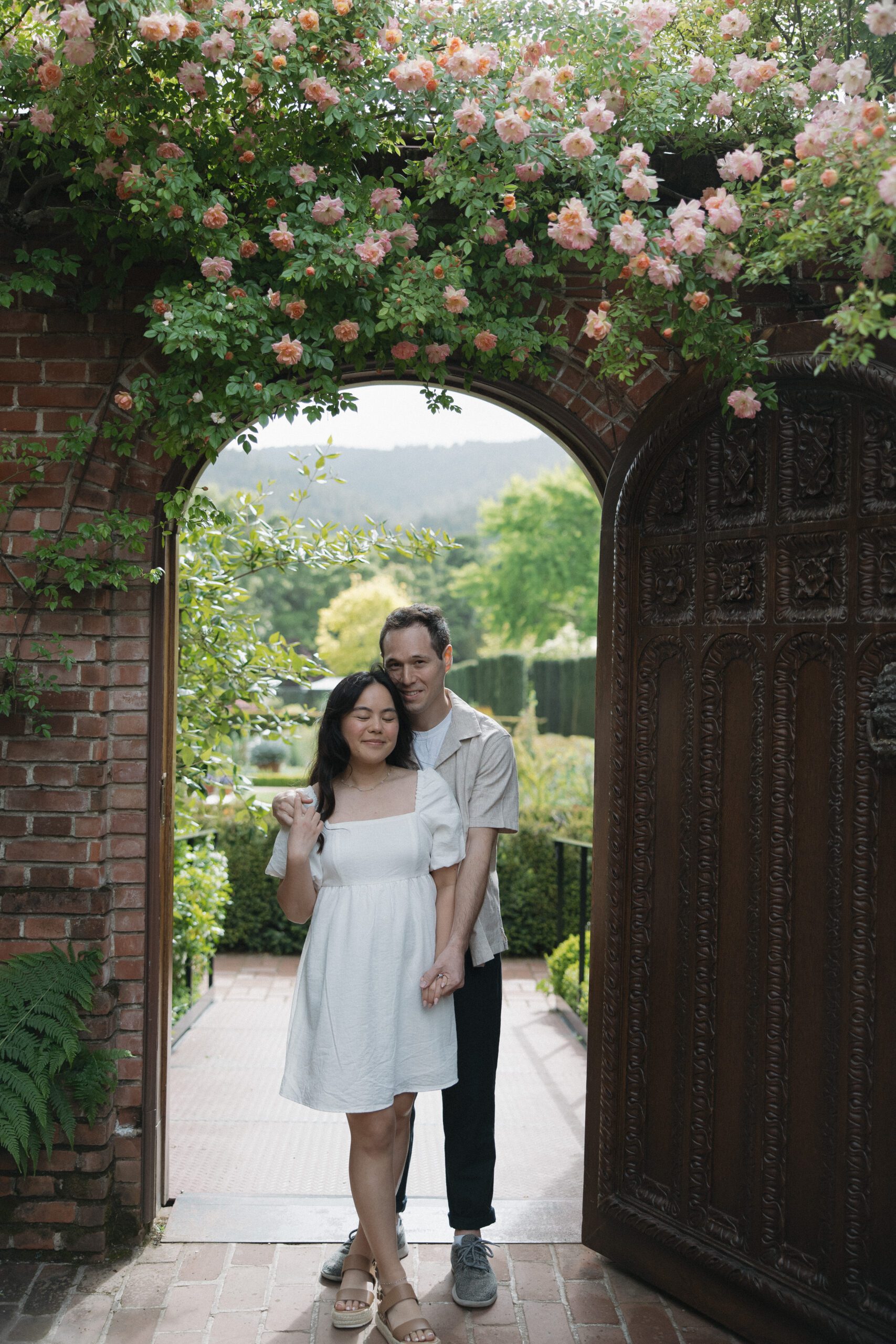 Engagement couple photo in arched doorway with flowers blooming above