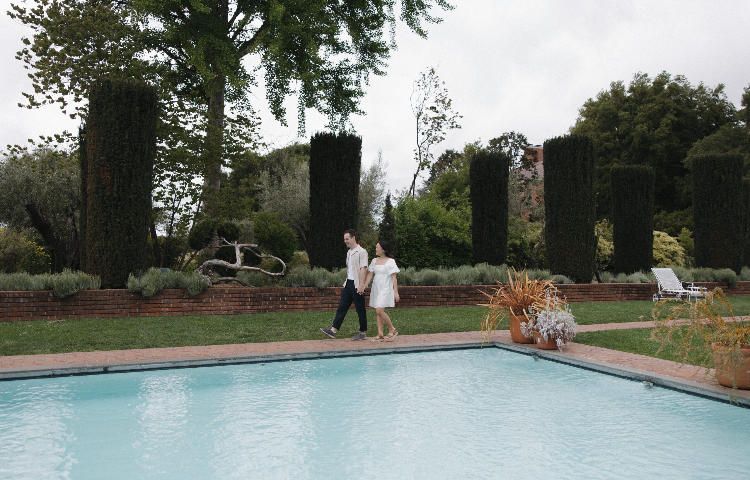 Couple walking by pool in vibrant garden engagement photos