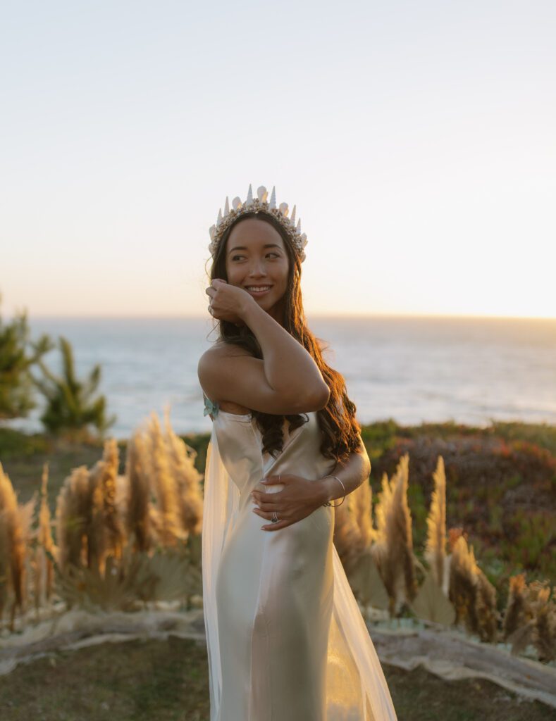 Bridal portrait from Bay Area wedding with bride wearing seashell crown and sunset on the ocean behind her