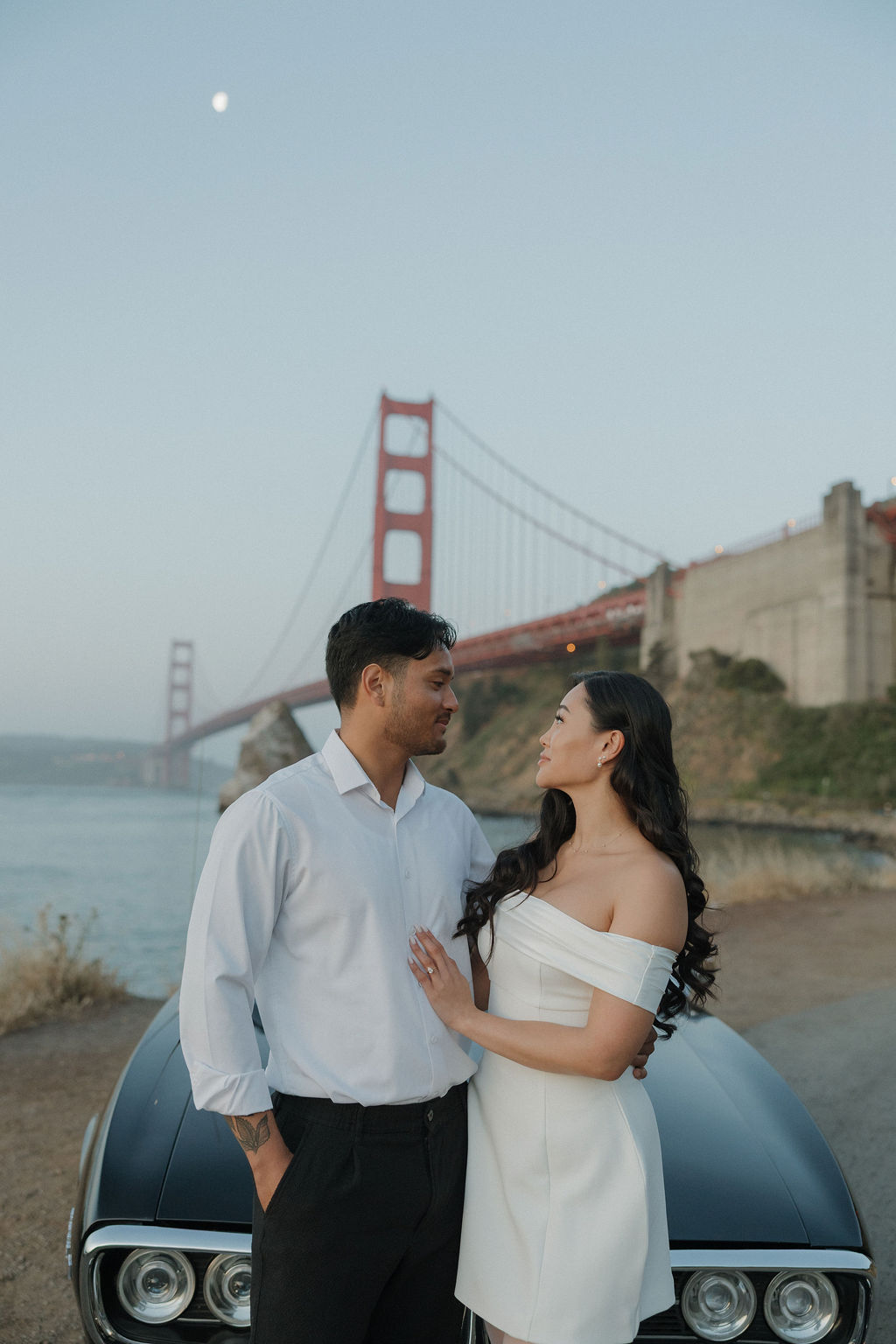 Engagement photos in front of Golden Gate Bridge with couple smiling at each other