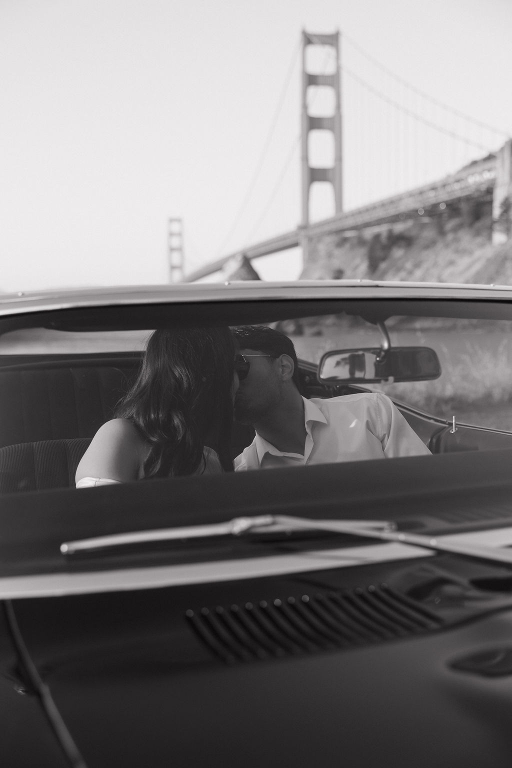 Black and white engagement photo of couple kissing in classic car