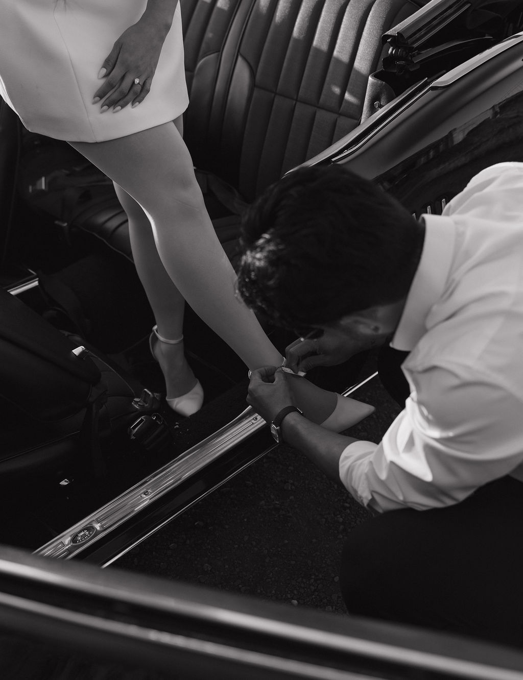 Man fixing his fiancees shoe during classic car engagement photos