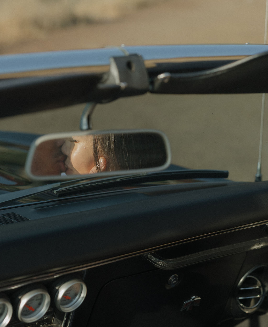 Editorial engagement photo of couple kissing in the car mirror of a classic car
