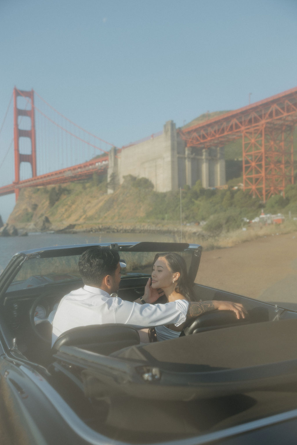 Groom holding bride's face in a classic car during Golden Gate Bridge photoshoot