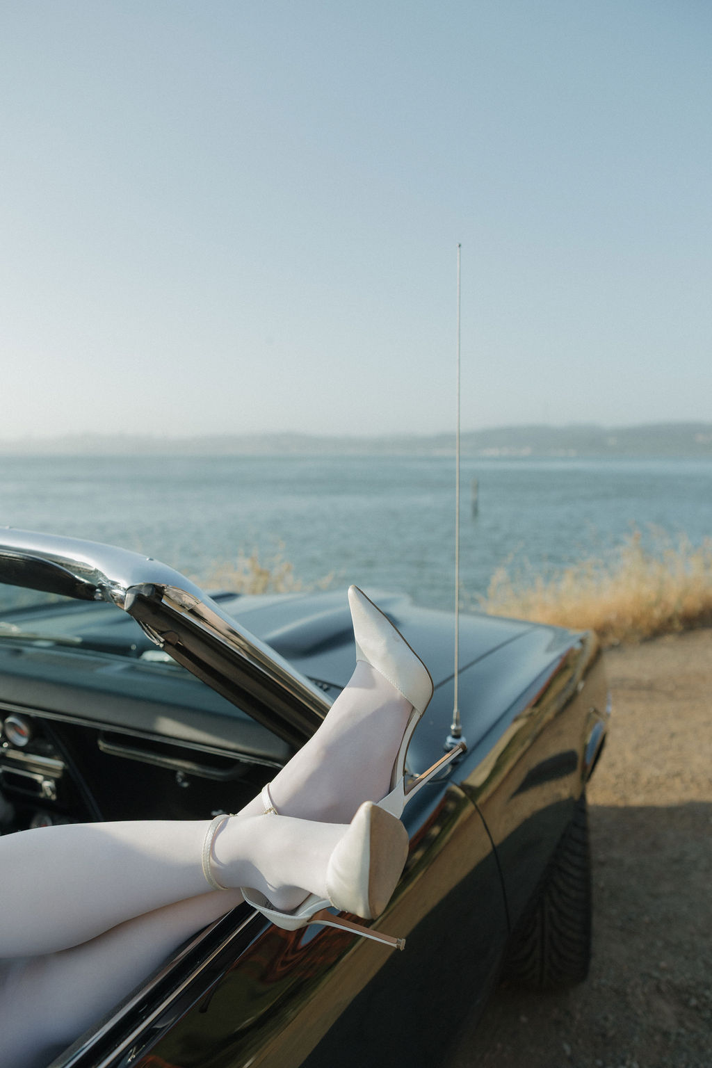 Bride kicking her legs out of a classic car to make an editorial engagement photo idea