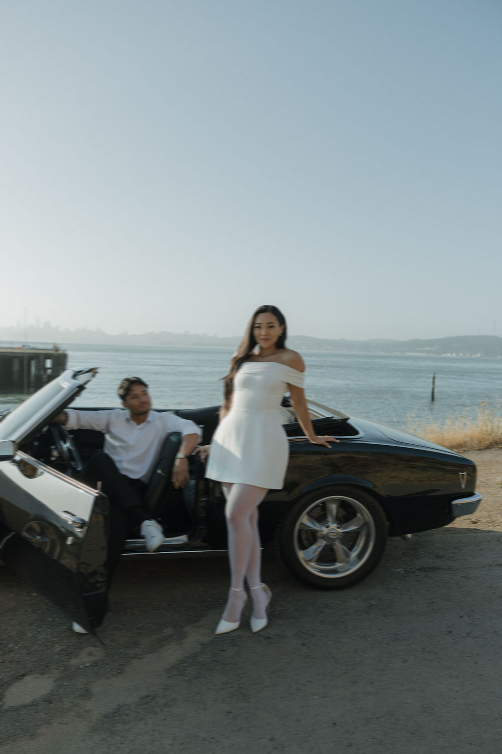 Bride leaned against classic car and groom sitting in drovers seat