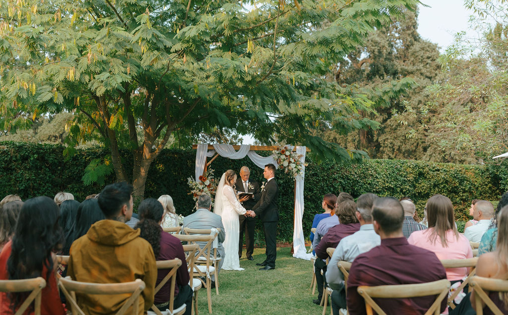 Bride and groom holding hands and praying during backyard wedding ceremony