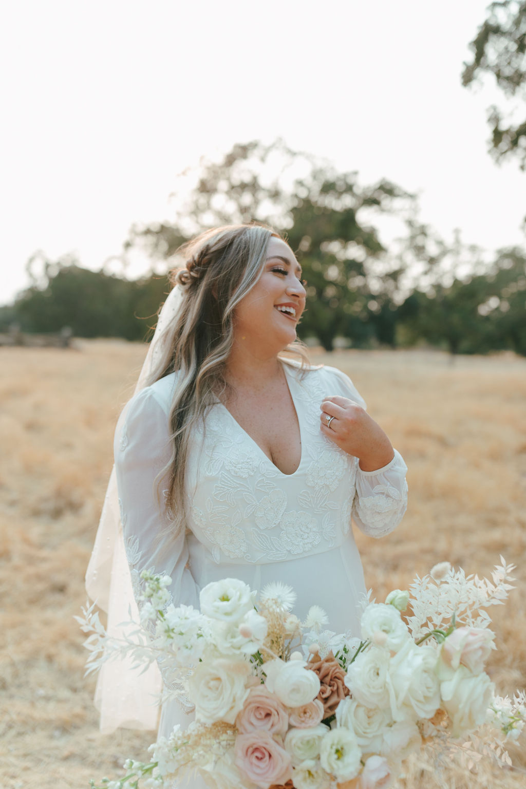 Bridal portrait of bride in her veil in a field holding baby pink and white wedding bouquet