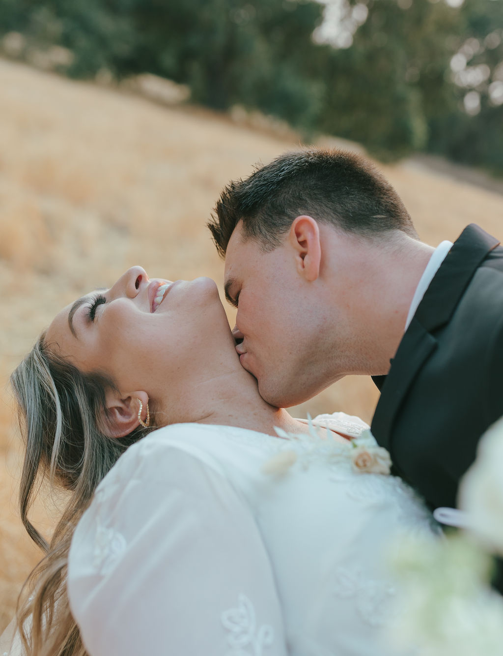 Groom kissing bride's neck and her throwing her head back laughing during wedding sunset photos