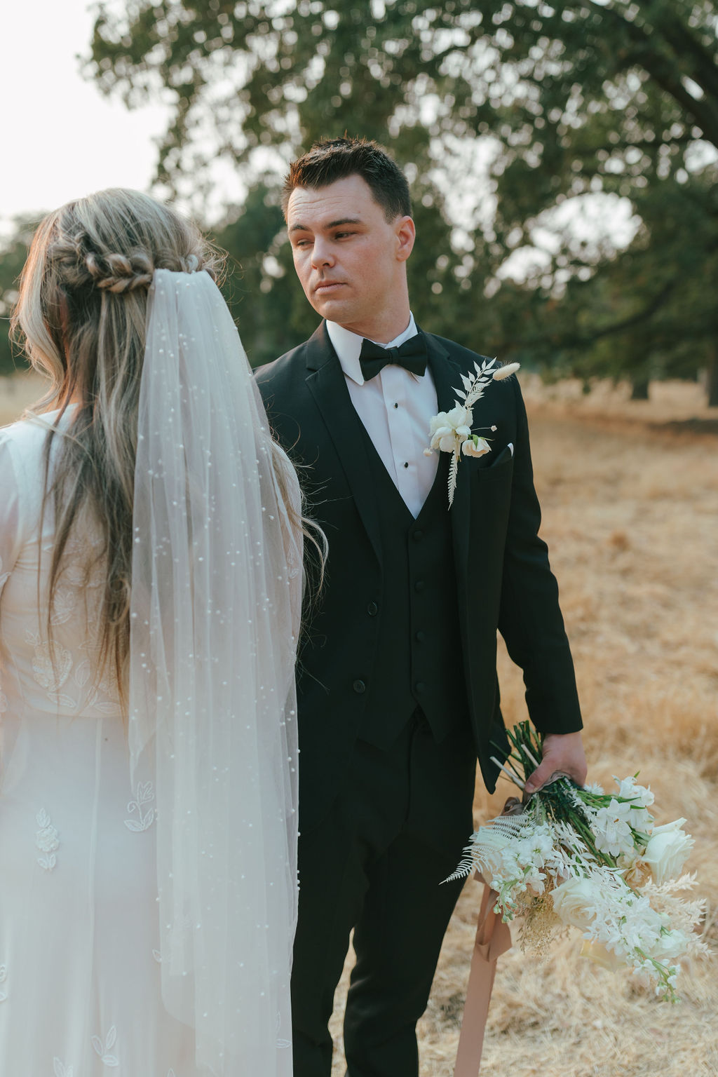 Editorial wedding photo of bride turned away from the camera showing her pearl veil and groom looking at her