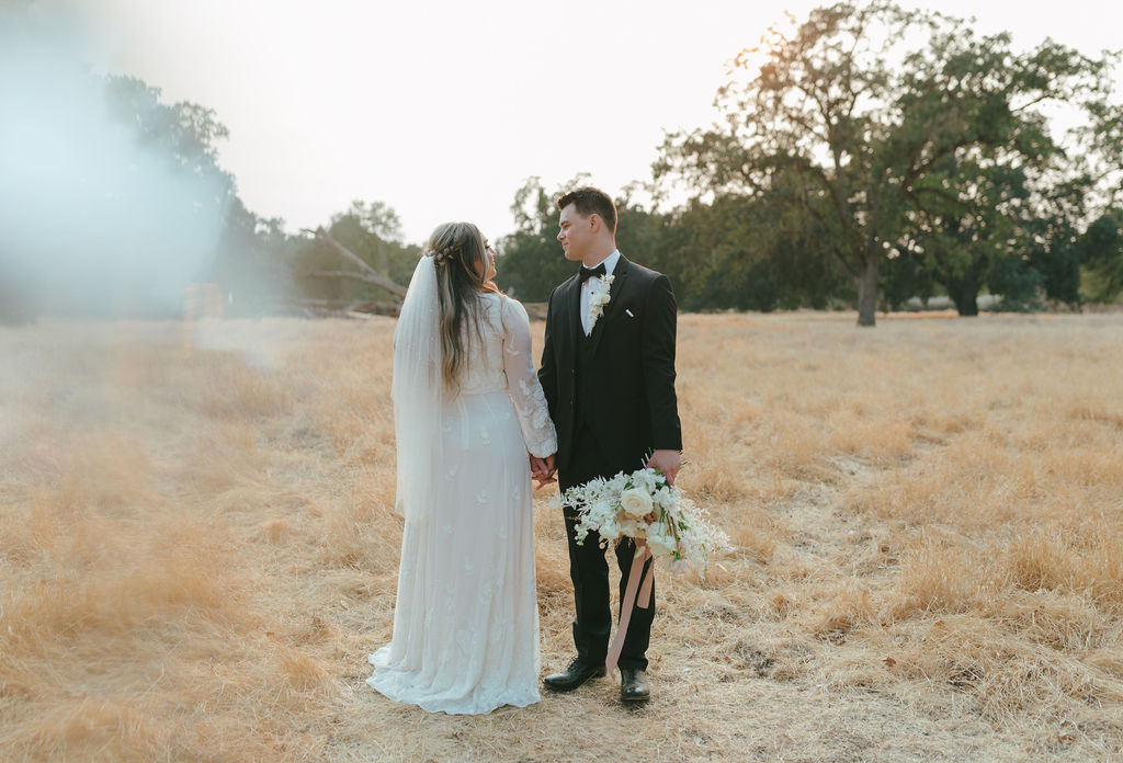 Editorial wedding photo of bride and groom in a field with bride facing away from the camera and groom looking at her