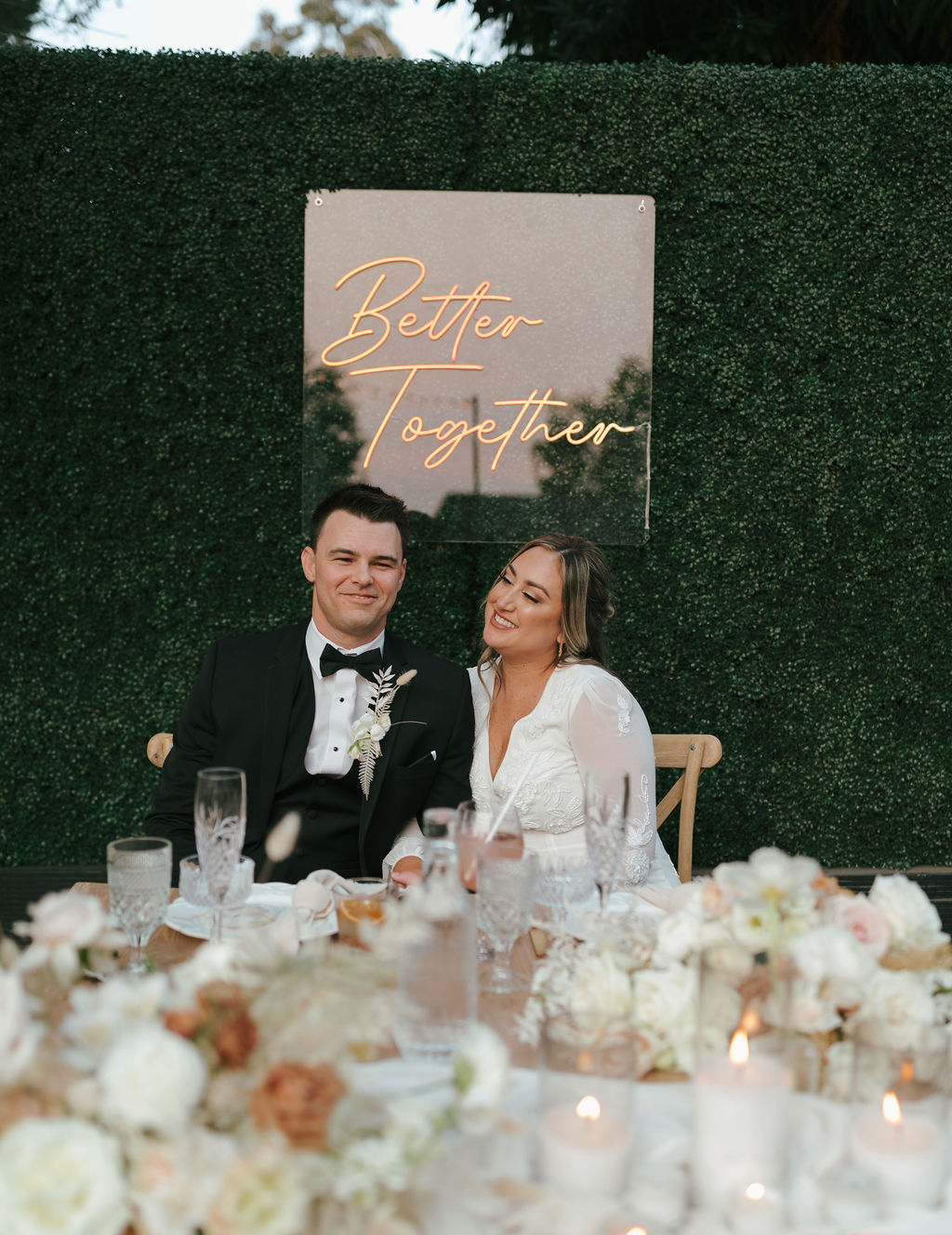 Bride and groom laughing at sweetheart table at outdoor California wedding reception with neon sign as nontraditional wedding idea