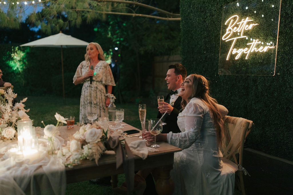 Bride and groom laughing from their sweetheart table during toasts at wedding reception