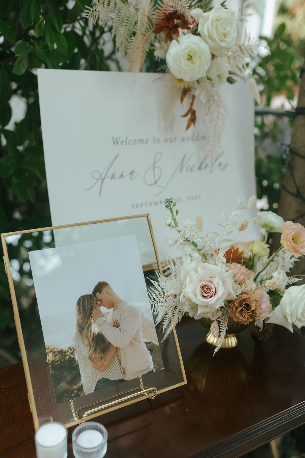 Photo of bride and groom's welcome sign and engagement photo in a frame beside it, with wedding flower decor