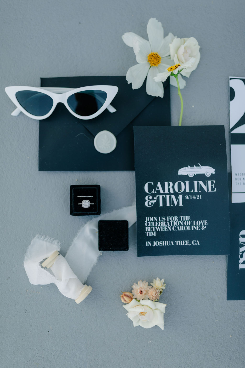 Black and white wedding flat lay with white wedding florals, black wedding invitations, rings, and bridal glasses
