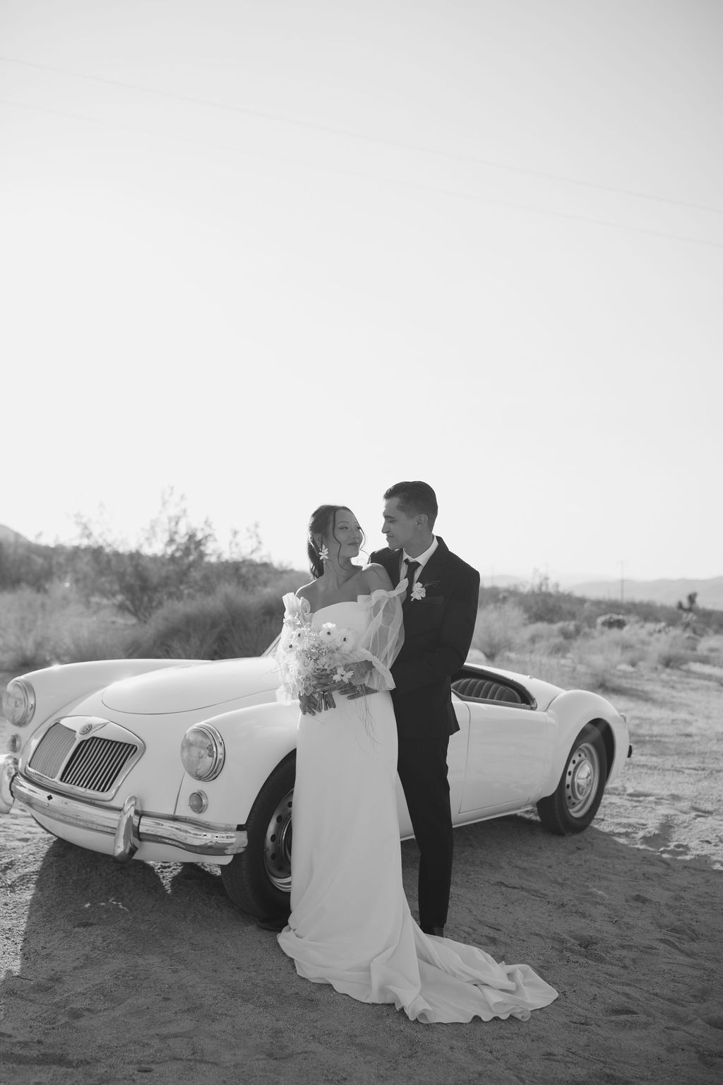 Black and white photo of couple in front of vintage car at Joshua tree wedding