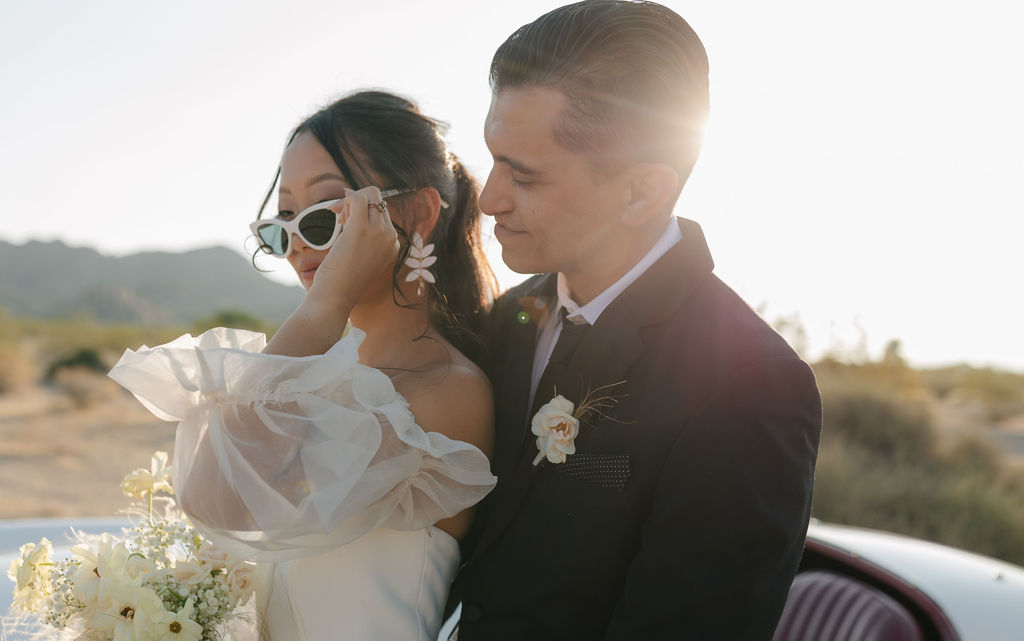 Bride holding her glasses and groom looking at her in Joshua tree wedding photos