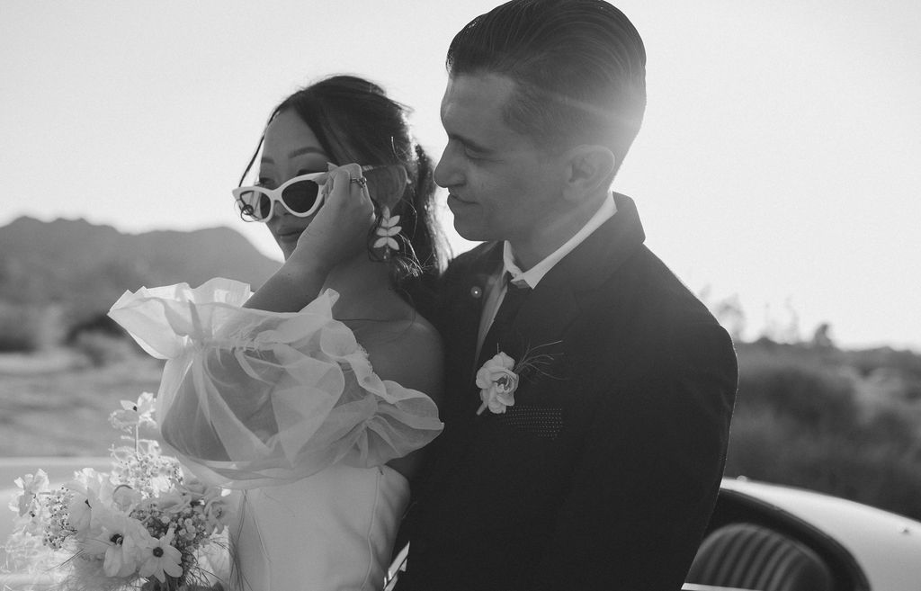 Black and white wedding photo of bride and groom with bride wearing sunglasses and groom smiling at her in Joshua tree