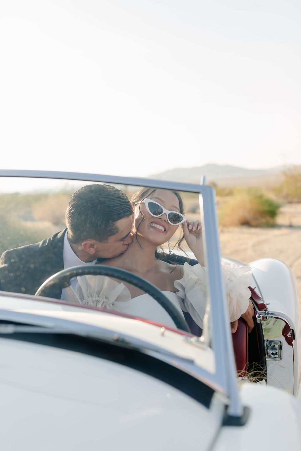 Brie and groom photo in a. vintage car with groom kissing bride's neck