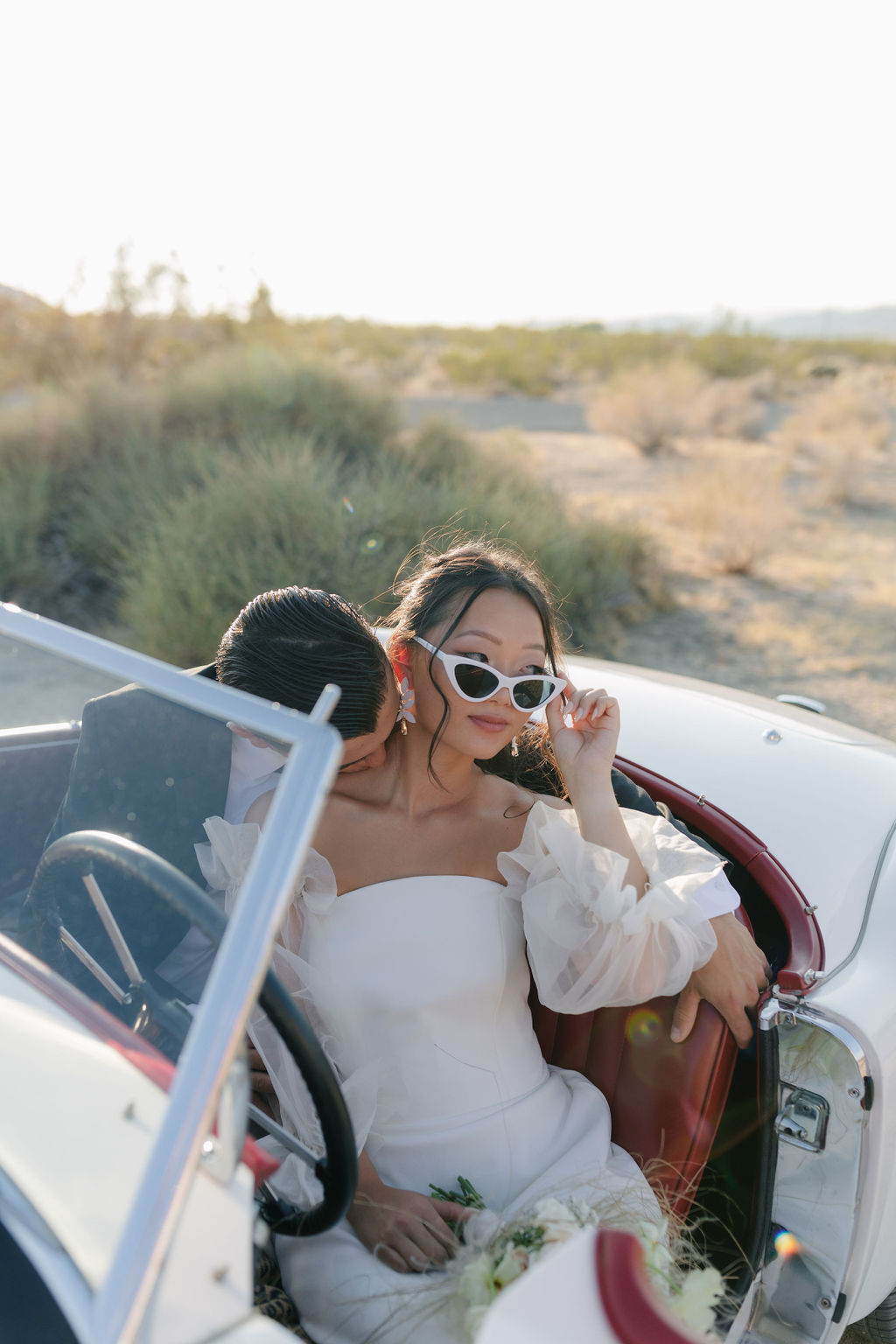 Bride and groom posing for photos in a vintage car at Joshua Tree elopement