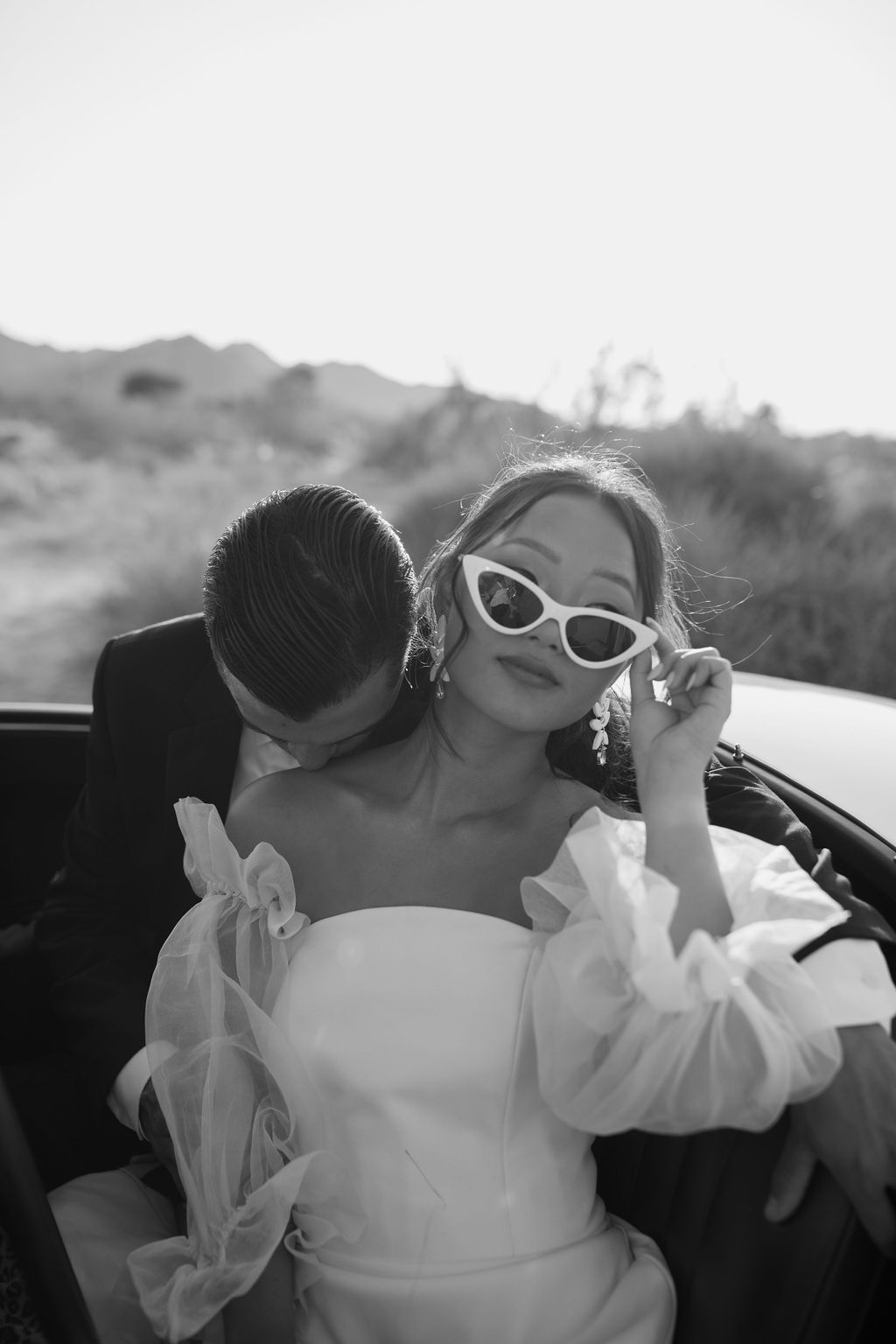 Black and white editorial wedding photo in vintage car with bride wearing glasses