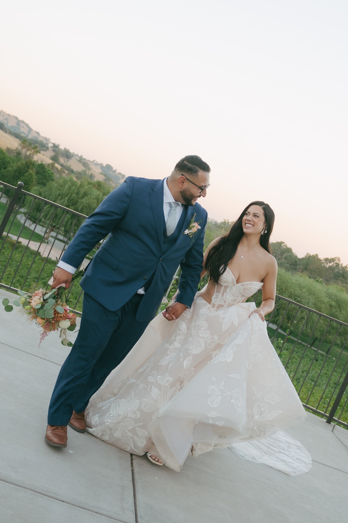 Bride and groom running towards the camera during sunset photos with groom holding wedding bouquet and bride holding her dress