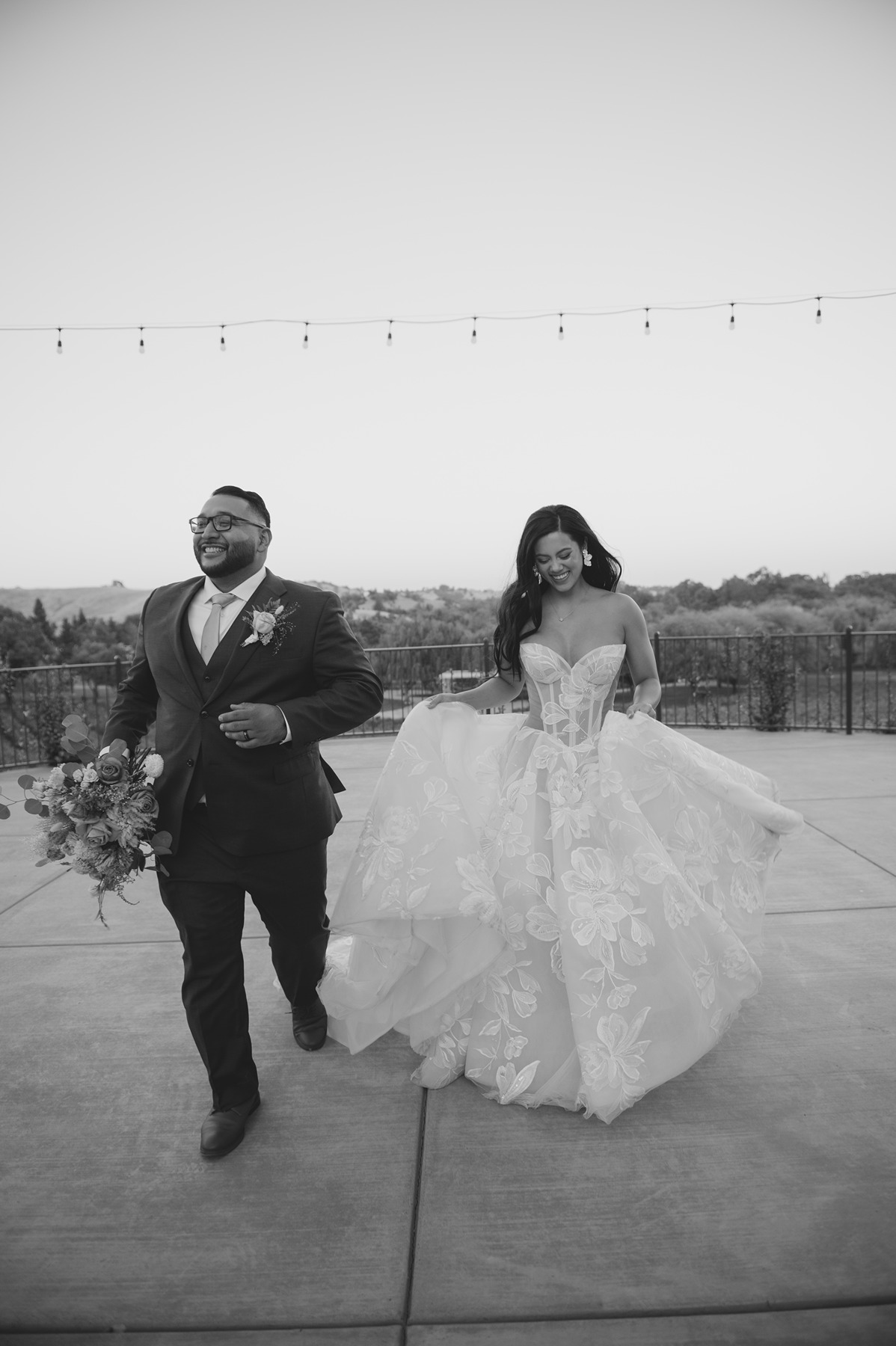 Black and white photo of bride and groom running towards camera