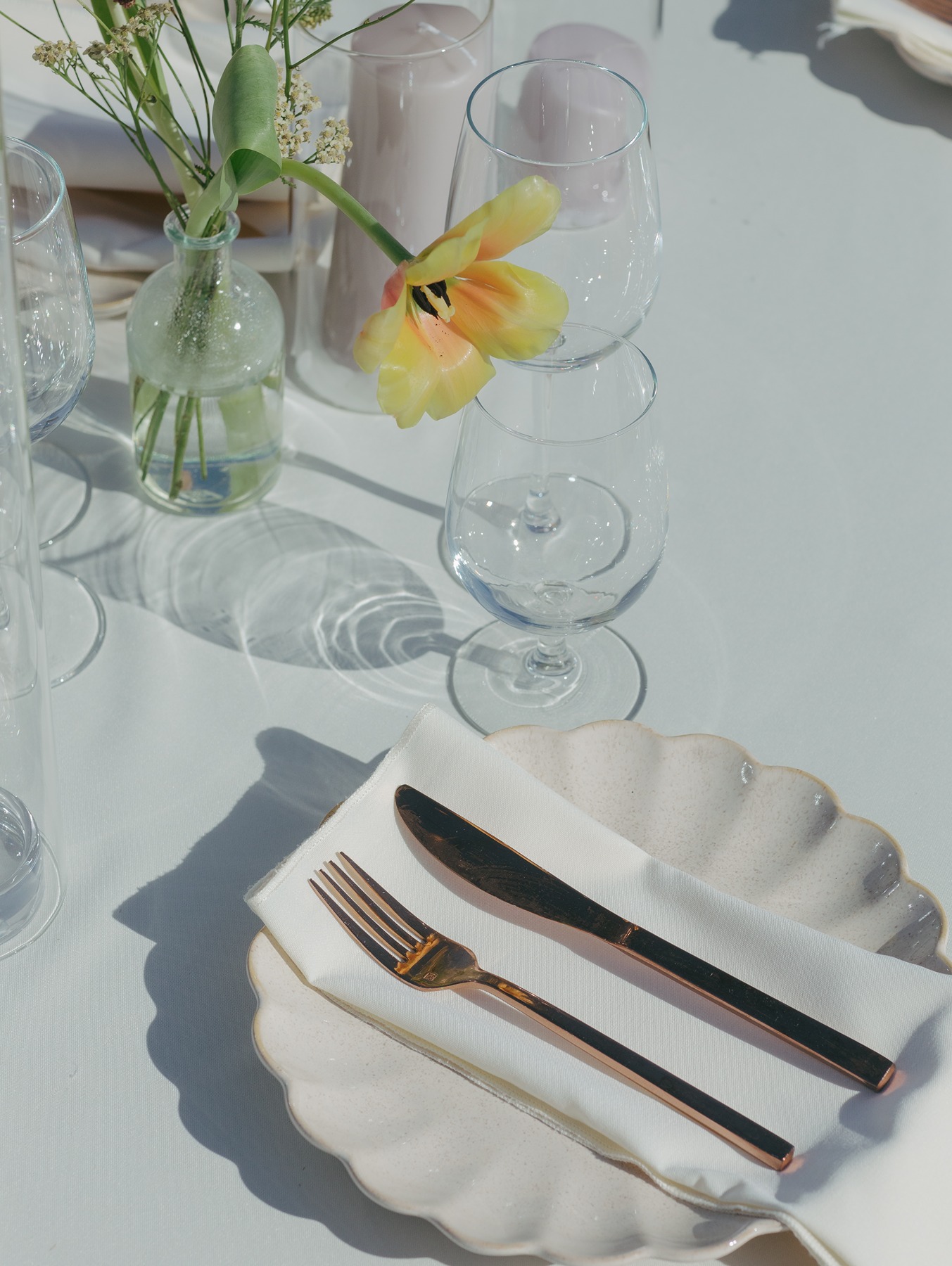 Wedding table setup with luxury wedding details, like rose gold flatware, a scalloped plate, and bud vases with wildflowers