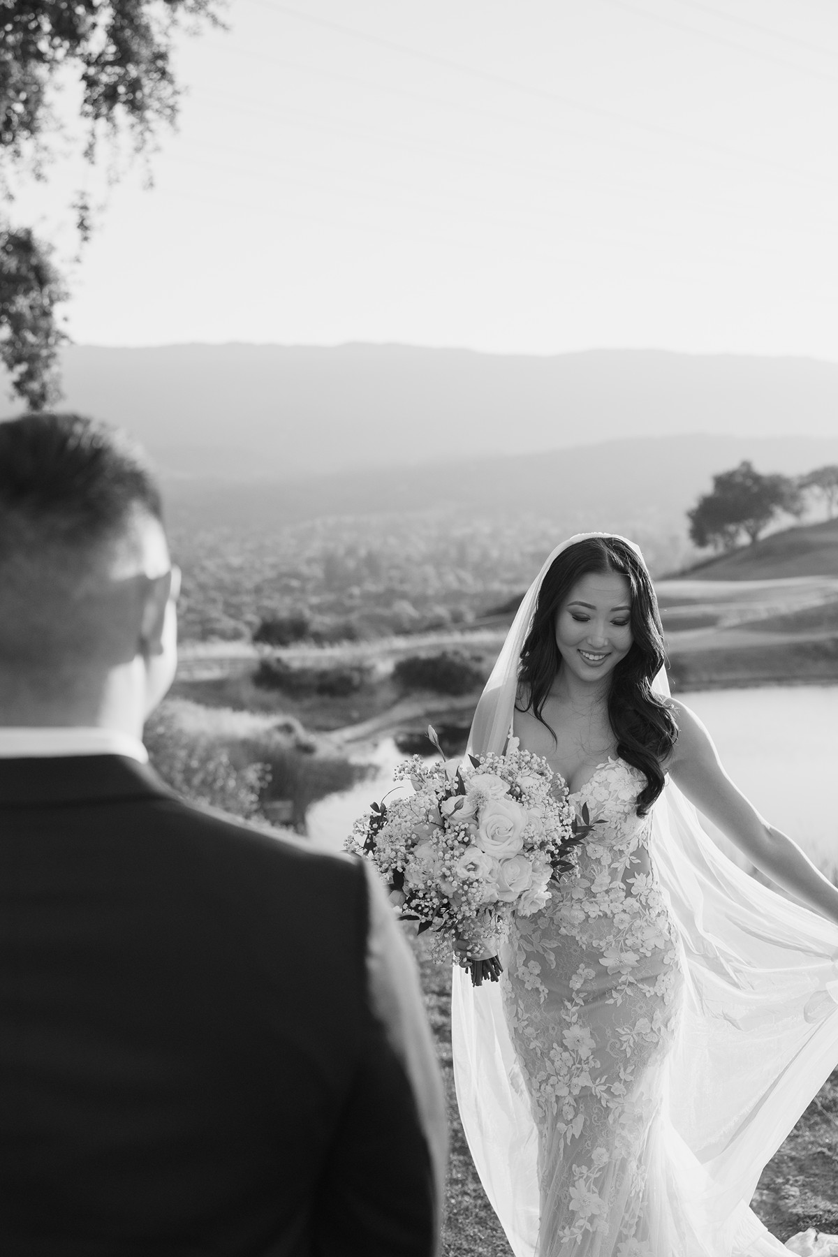 Black and white photo of groom staring at bride who is dancing in her statement veil