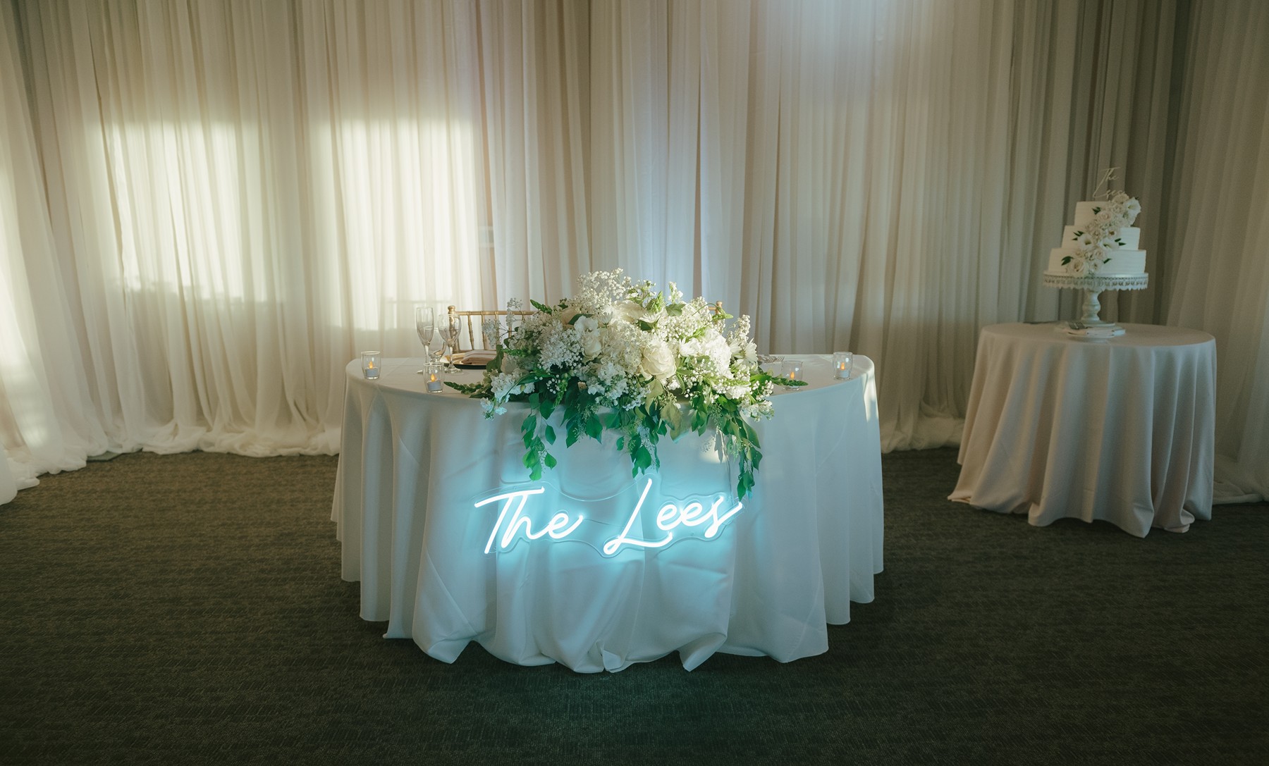 Sweetheart table setup with a neon sign lit up on the front and white floral centerpieces