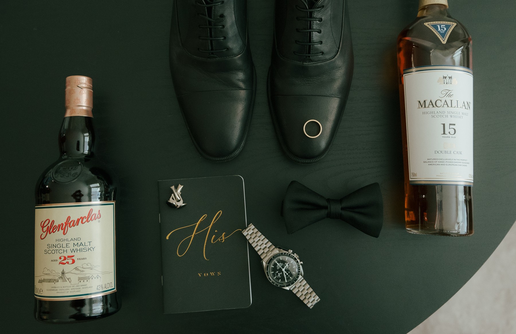 Groom's wedding details in a flat lay, with his shoes, bowtie, whiskey, watch, and cologne