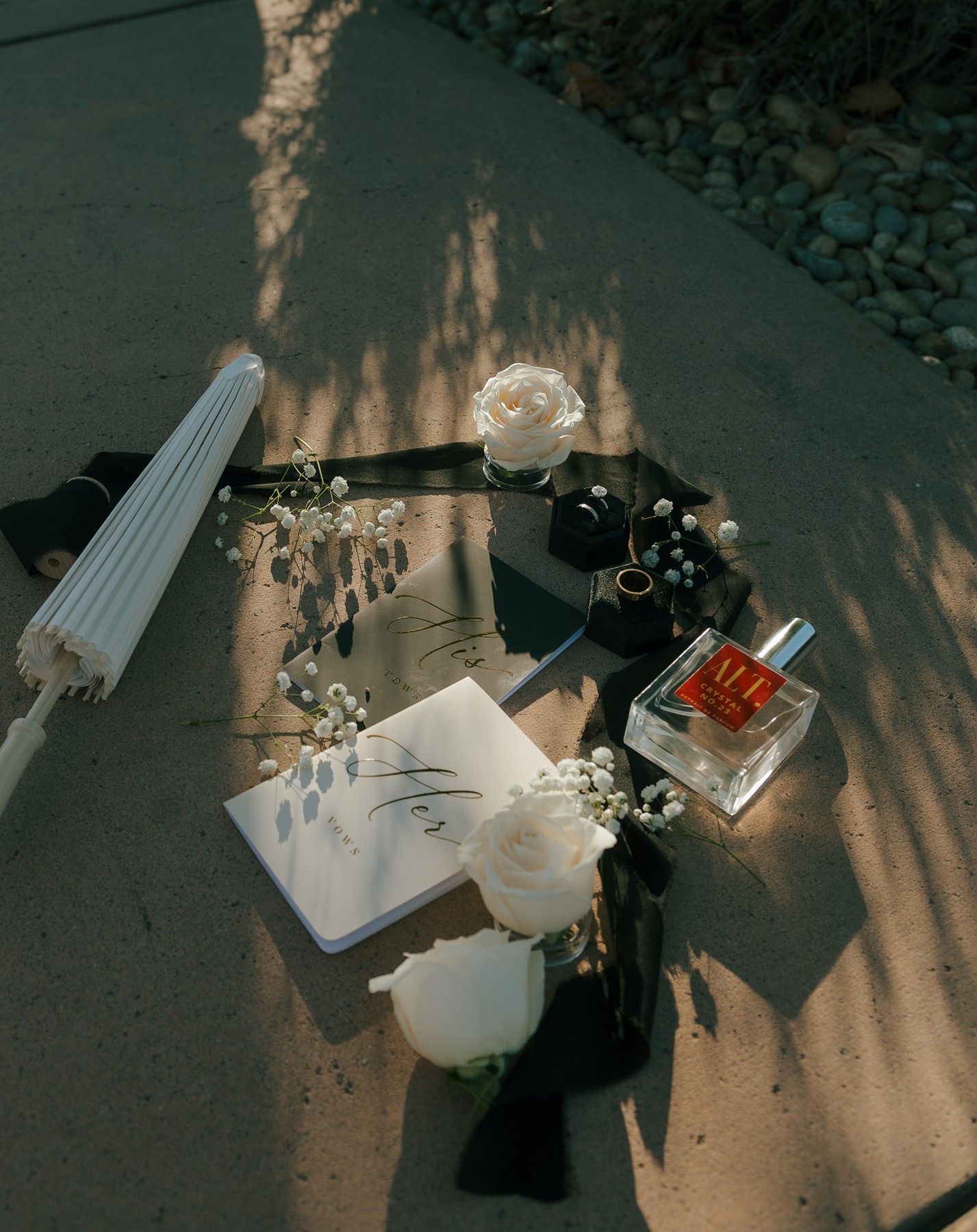 Wedding flat lay with a parasol, vows, rings, flowers, and cologne
