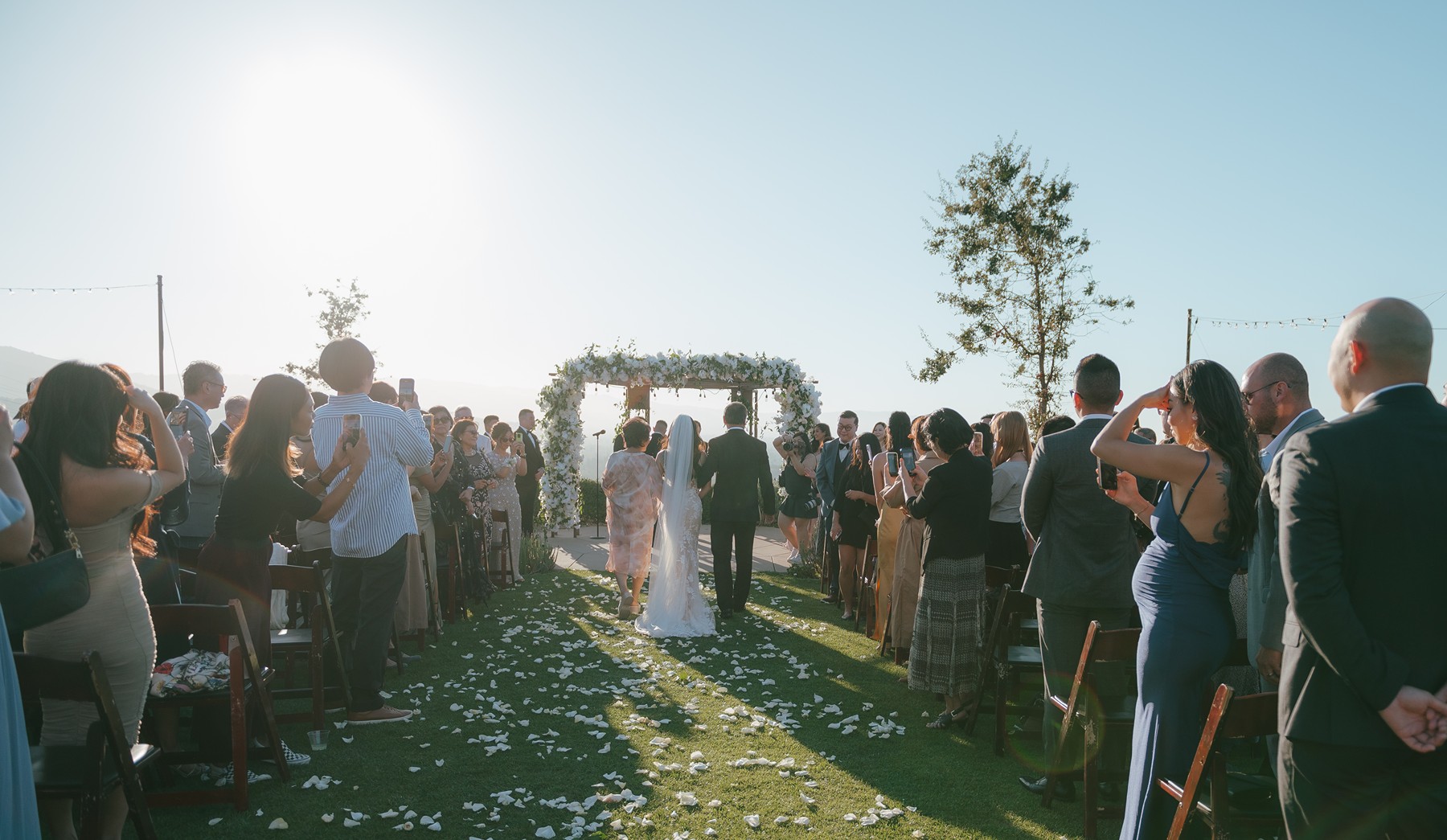 Bride'a parents walking her down the aisle at a sunny wedding